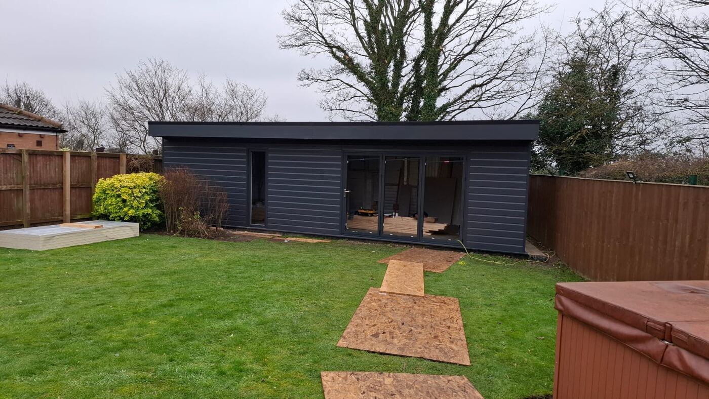 Dark clad garden room at the end of a lawn
